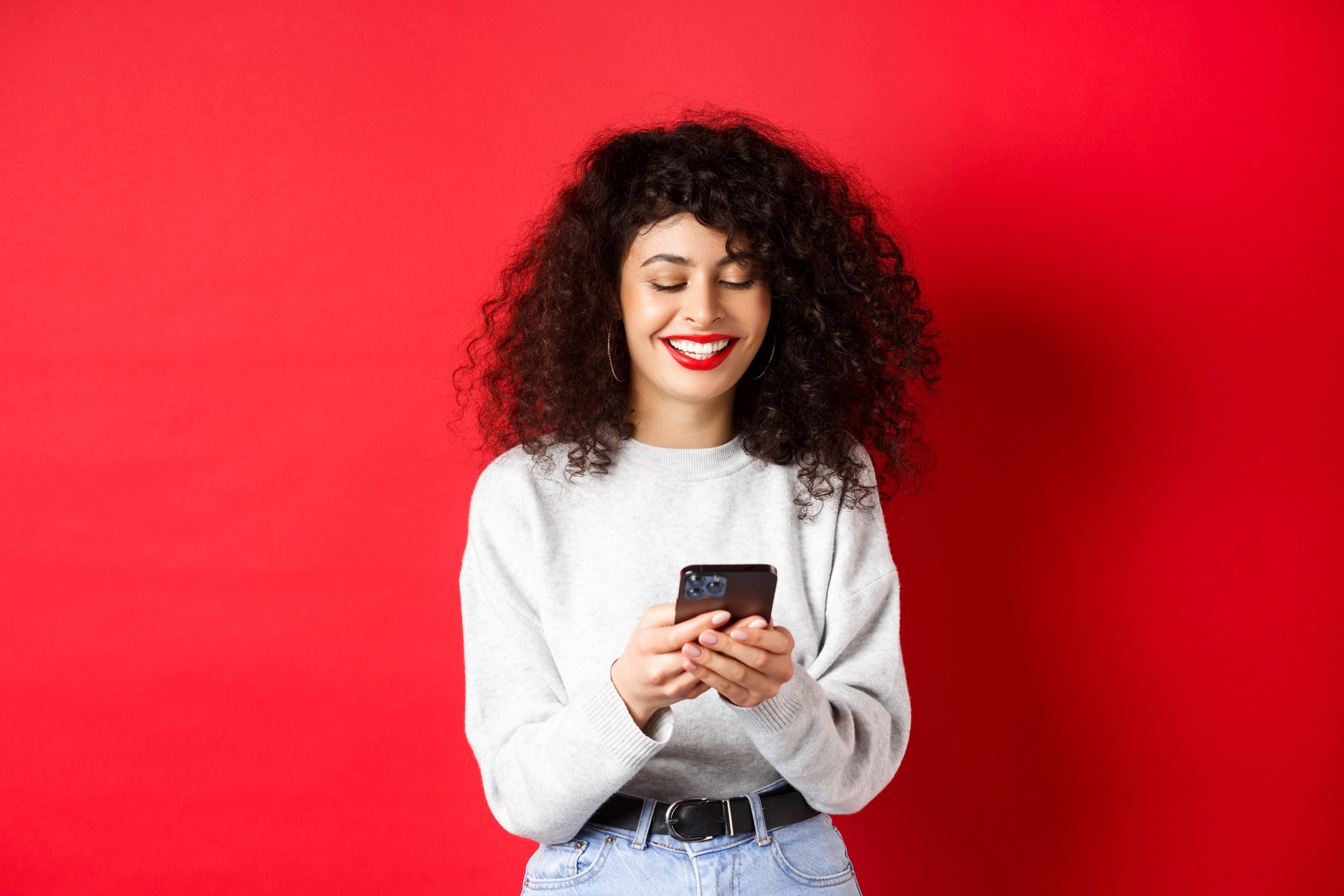 Happy Positive Girl Chatting on Phone, Reading Message and Smiling, Using Social Media App, Standing on Red Background
